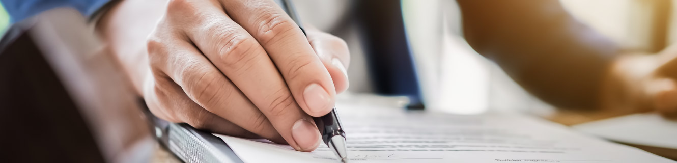 Close of of hand holding a pen to paper document.