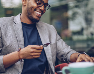 Happy man holding a credit card in one hand at an outdoor cafe.