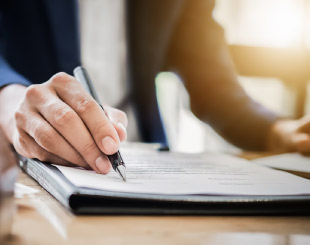 Close up of a business man's hand holding pen over paperwork.