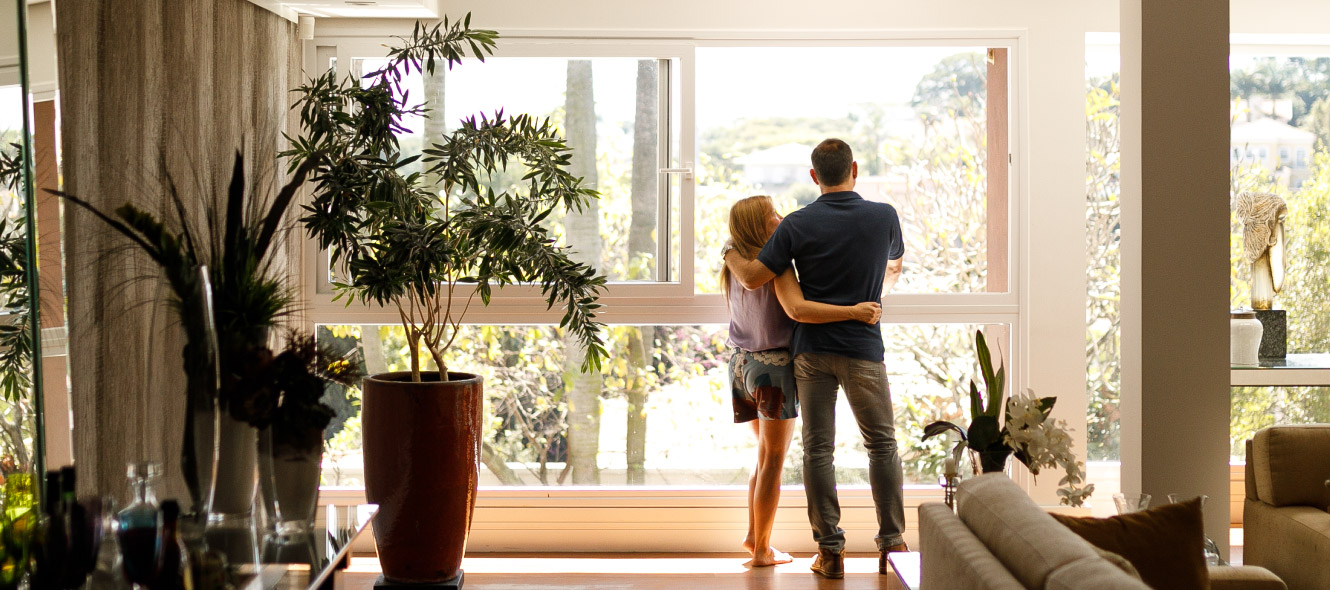 Man and woman in each others arms looking out their living room window.